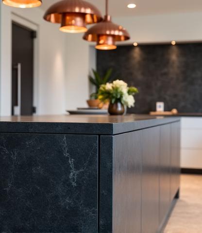 Cucina residenziale elegante con isola centrale in pietra scura e illuminazione a sospensione in rame.