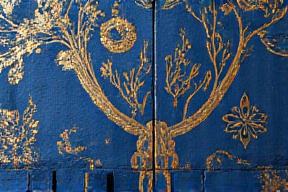 Parete rivestita con carta da parati a motivo botanico dorato e blu scuro.